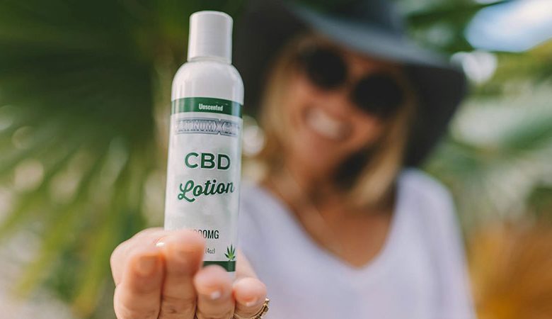 a woman wearing a black hat and a white top showing a white plastic bottle of CBD lotion on top of her palm