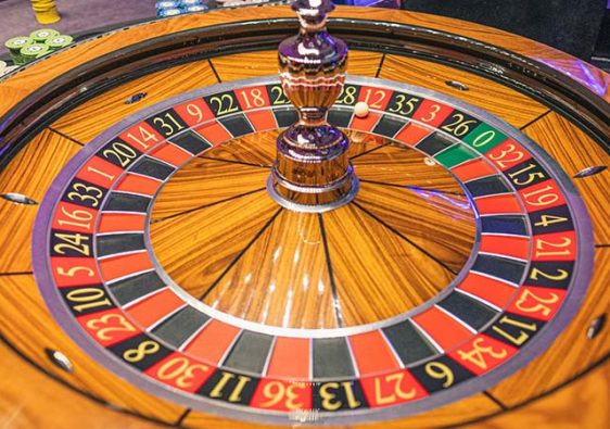 a brown wooden roulette and several stacked casino chips beside it