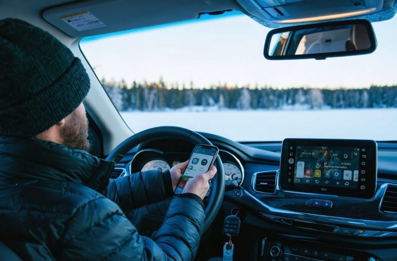 Driver in a midsize SUV holds a smartphone as if applying for auto financing, with car keys on the console, parked beside a snowy lakeside lined with boreal pines at golden hour.