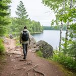 “A mixed boreal forest trail with rocky outcrops and a hiker from behind, with Van Horne Lake visible through trees near Dryden, Ontario.”